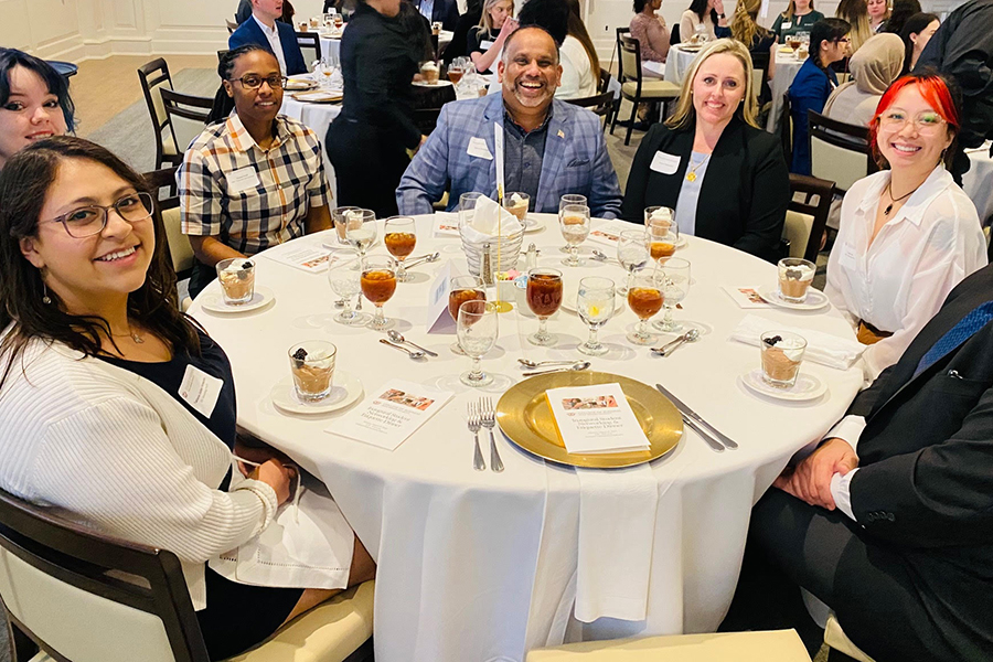 seven students and professionals sit at a dinner table in a ballroom