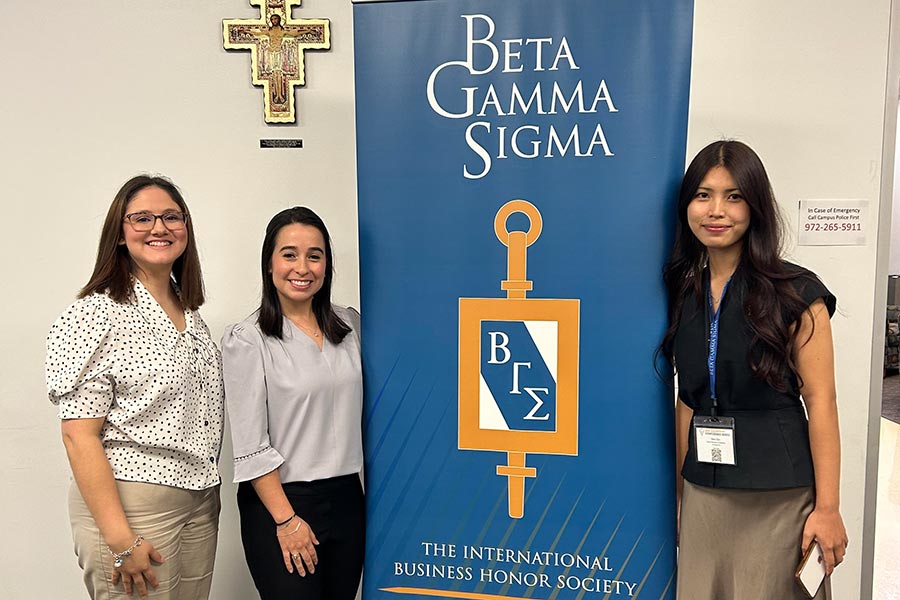 three students stand next to a blue Beta Gamma Sigma banner