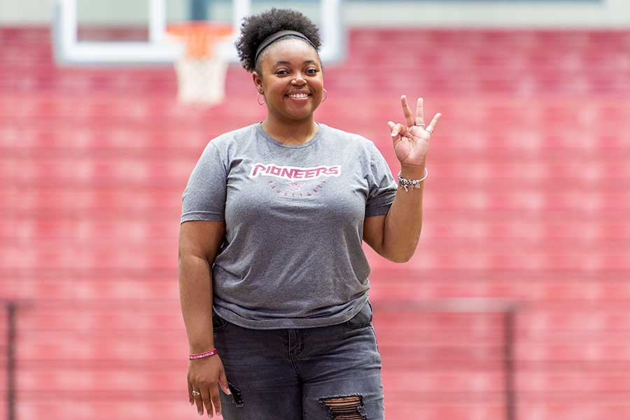 TWU student, Lauryn Johnson, holds up the university hand sign in the basketball gym