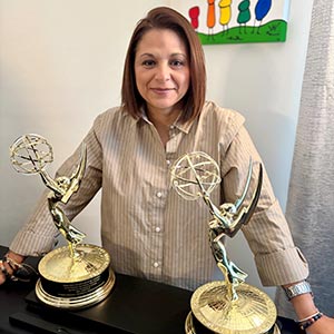 Vanessa Miranda stands with two Emmys in front of her on a table