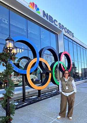 Vanessa Miranda stands in front of large Olympic rings on the front of NBC Sports office