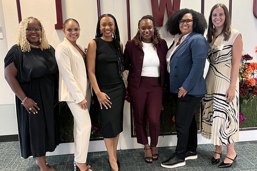 six women stand in front of wall with TWU initials