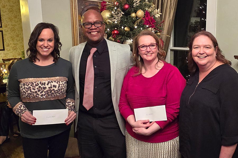 four people, including two TWU students, stand in front of Christmas tree