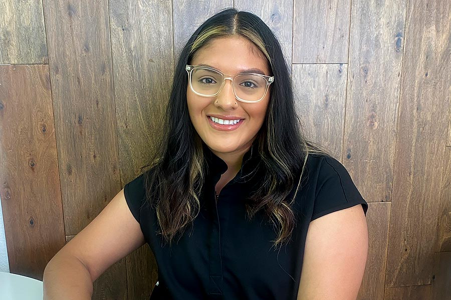 a woman in a short-sleeved black shirt sits in front of a wood-panel wall