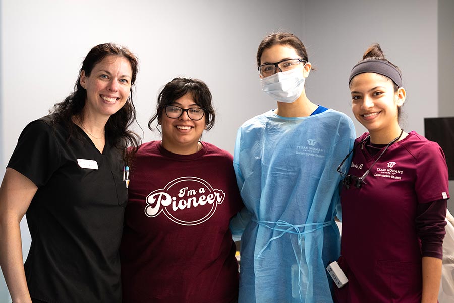 a faculty member in black scrubs stands with three dental hygiene students