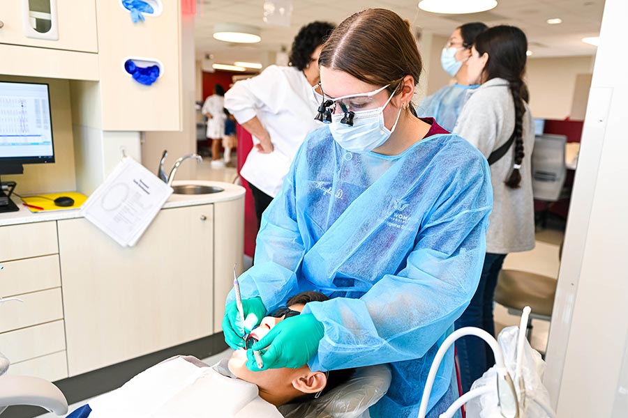 a TWU dental hygiene student uses dental equipment to inspect a patient's teeth
