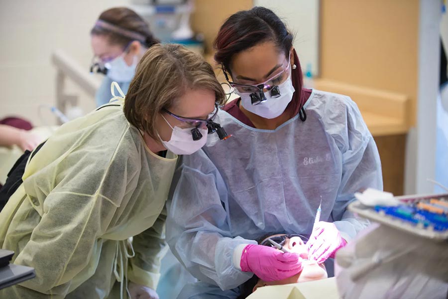 faculty member looks over shoulder of dental hygiene student working on a dental patient in chair