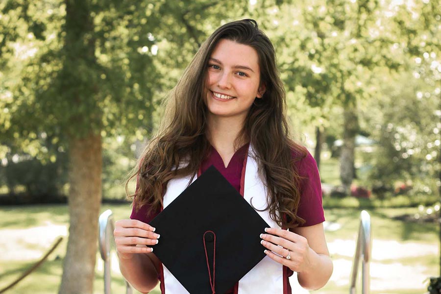 TWU dental hygiene graduate holds a graduation cap in front of her outdoors