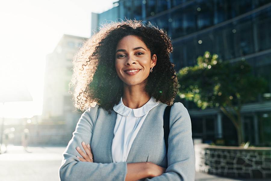 A woman outdoors in a city setting and wearing professional dress.