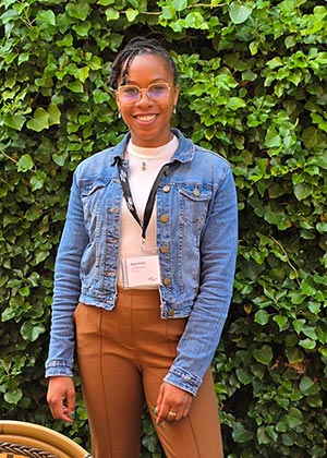 Kesia Derilus stands in a jean jacket in front of an ivy wall