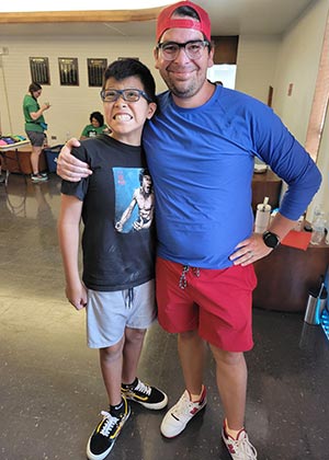 a camper in dark blue shirt stands next to his coach in light blue shirt 