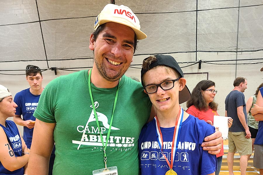 Coach in green shirt stands next to camper in blue shirt
