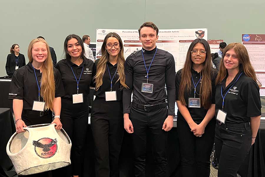 six students dressed in black stand in front of project poster