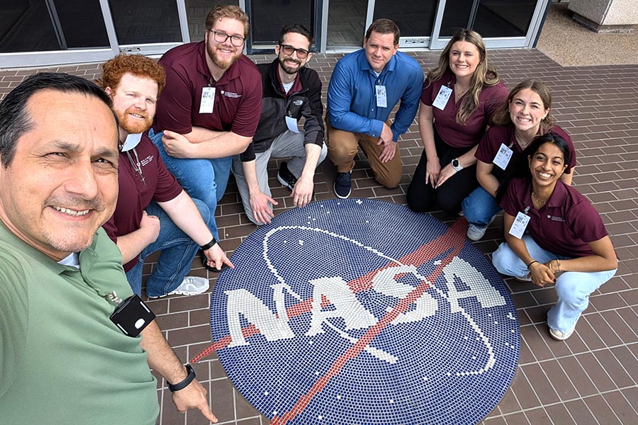 eight people crouch around a NASA logo on the ground