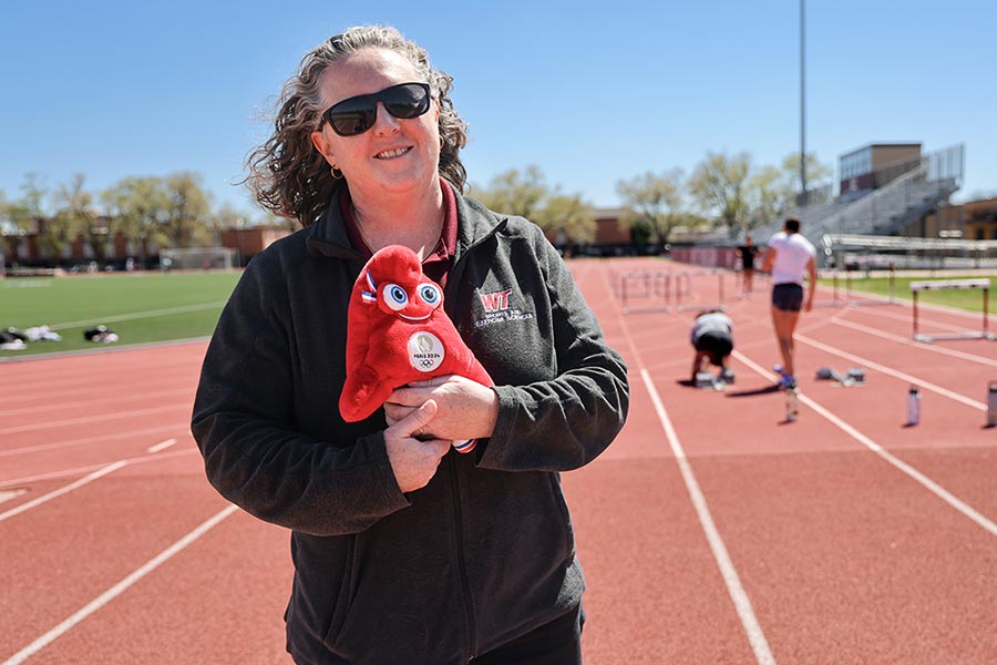 TWU alumna standing on a track holding a small Paris Olympics stuffed mascot