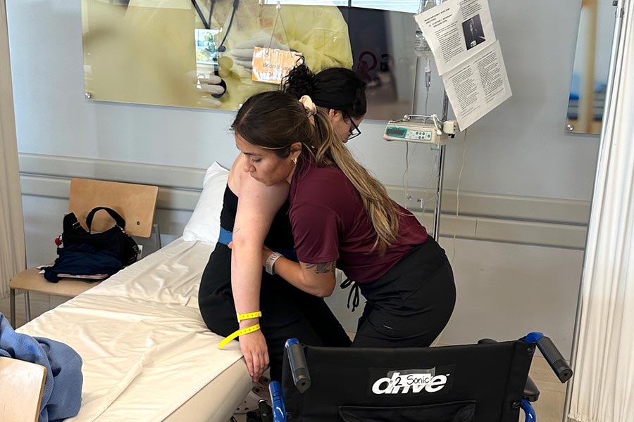a TWU student in a maroon student holds onto a patient as she lowers her to a bed