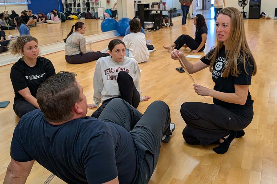 an OT professor holds a goniometer while talking to three students in a dance studio