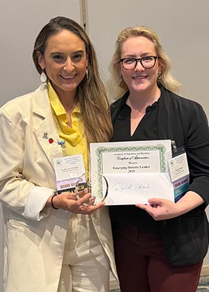 Rachel Poland, in a black shirt, receives a certificate from a board member