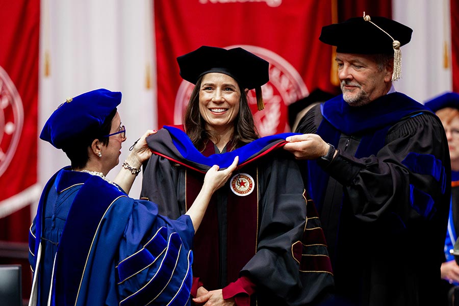 two faculty members place a hood on TWU PhD student at commencement