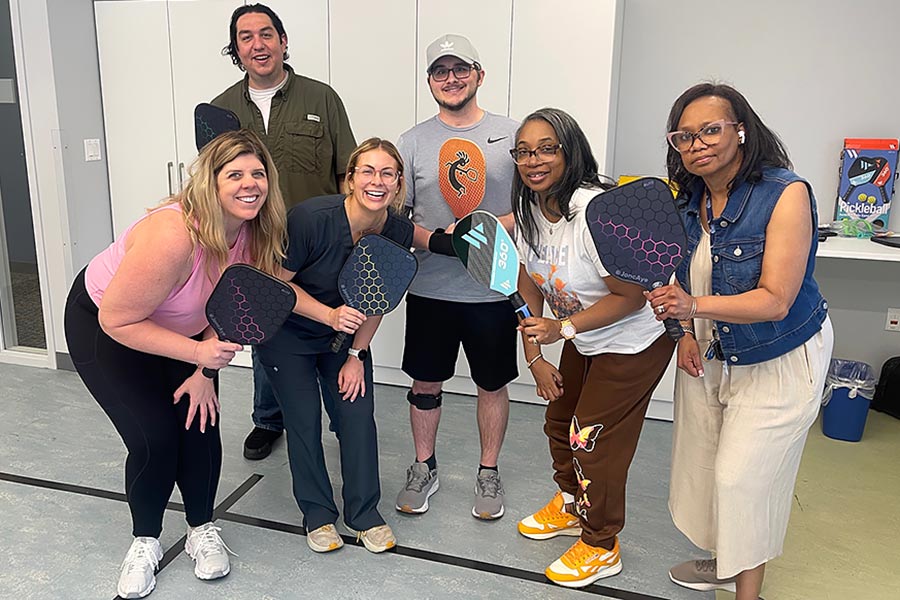 five Stroke Center clients and an OT student stand in semi-circle with paddles in classroom 