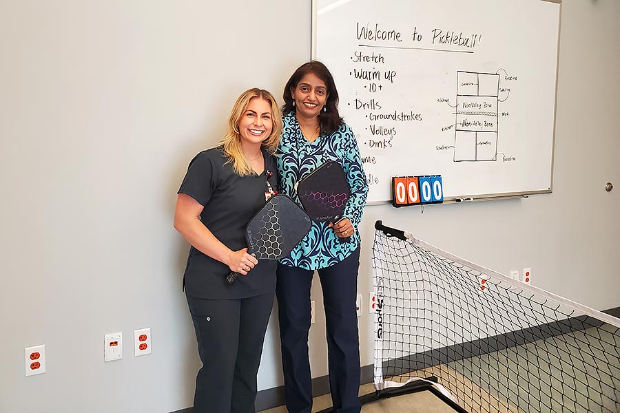 Natalie Mackie and Asha Vas stand next to one another, holding paddles, in a classroom