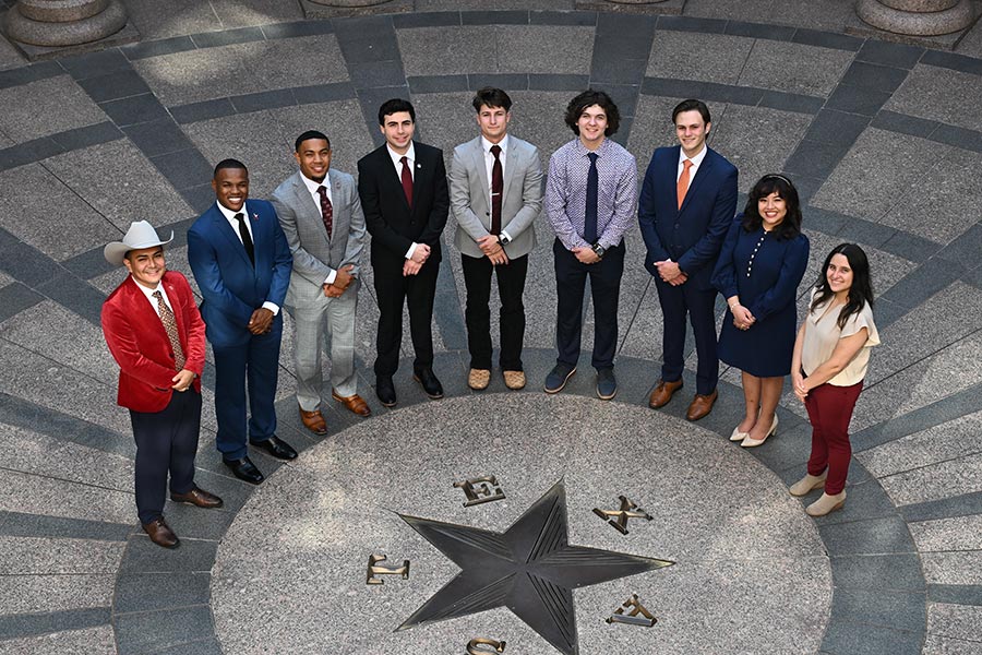 nine students stand around the top of a circle on the floor with a star in the middle with the words Texas