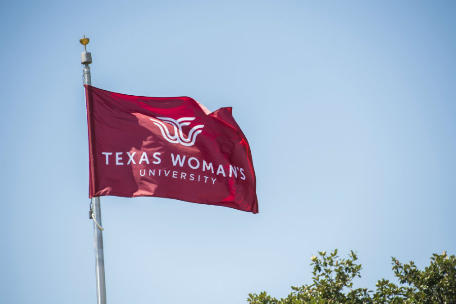A maroon flag flying on TWU's Denton campus with the logo in white.	