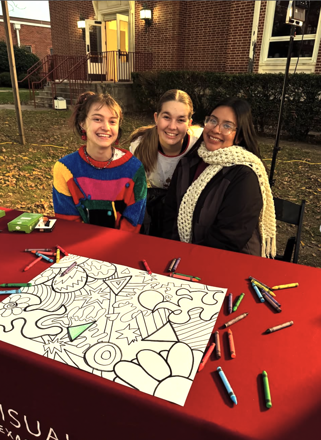 3 NAEA Preservice Pioneers, sitting at a table with a coloring page and crayons during Circle of Light, December 2024. NAEA Preservice Pioneers are an Art Education Student Organization.