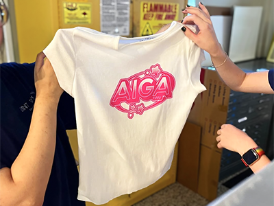 Two students hold up a T-shirt they silkscreened with the Aiga TWU logo, during a screen printing workshop